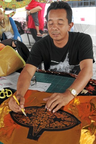 Wau maker Kalimi Abdul Hadi demonstrating the way he carves the patterns to make ‘wau’