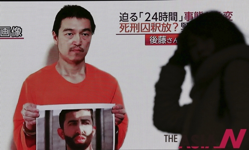 A passerby is silhouetted against a large TV screen broadcasting a news program Wednesday, Jan. 28, 2015 in Tokyo reporting on a video posted on YouTube by jihadists on Tuesday, Jan. 27, that purports to show a still photo of Japanese hostage Kenji Goto holding what appears to be a photo of Jordanian pilot 1st Lt. Mu'ath al-Kaseasbeh.