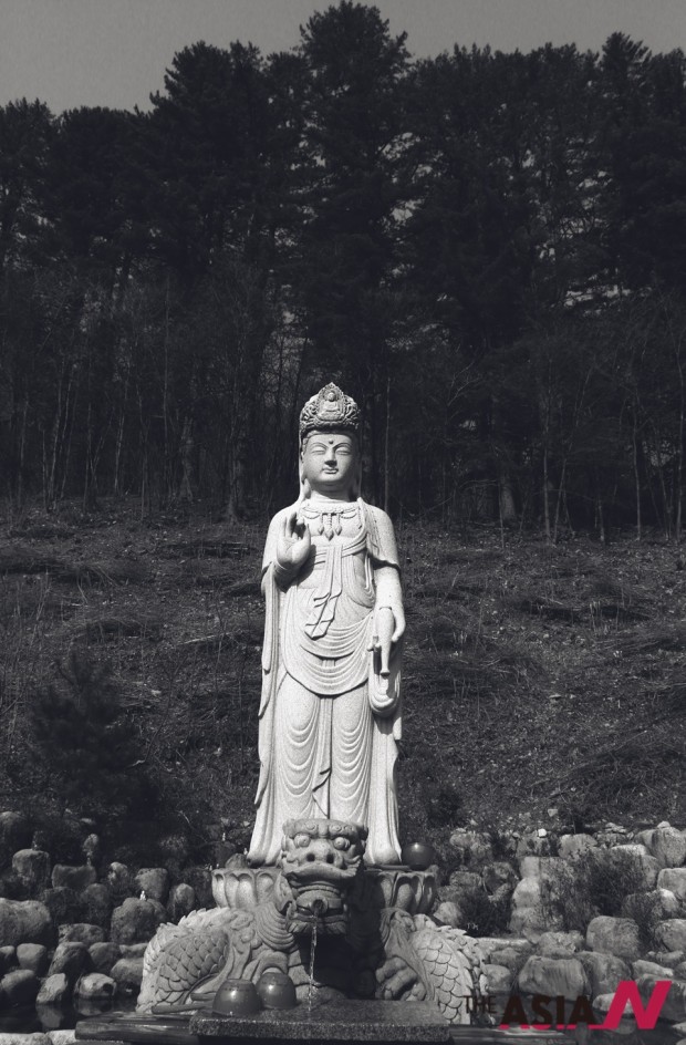 The majestic statue of Buddha stands tall at Baekdam temple, surrounded by the woods in the back and the temple and tourists on the other sides.