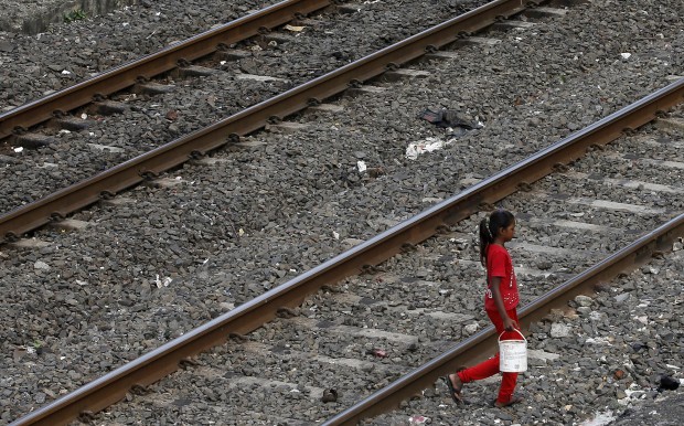 An Indian girl holds a can filled with water and walks past railway tracks to defecate in the open in Mumbai, India, Tuesday, June 30, 2015. (AP Photo)