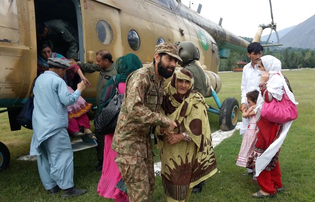 In this photo taken on Thursday, July 23, 2015, Pakistan army officers help stranded people evacuate from flood-hit areas in Chitral, Pakistan. Pakistani authorities say flash floods, triggered by monsoon rains, have killed 12 more people across the country, bringing the overall death toll since early last week to 15, as rescuers struggle to move those stranded to safer places. (AP Photo/Sherin Zada)