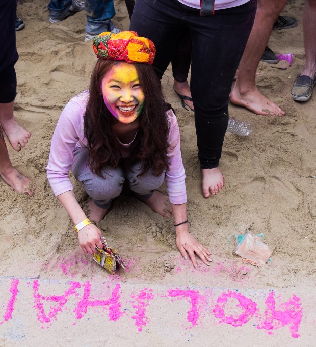 A girl writes 'Holi hai' (It's Holi) with colors on the beach.