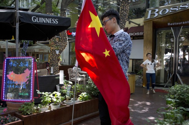 A worker of a restaurant bar prepares to hoist a Chinese national flag near a drawing of the country with the words "China, South China Sea, China's territory right does not need arbitration" in Beijing, Wednesday, July 13, 2016. China warned other countries Wednesday against threatening its security in the South China Sea after an international tribunal handed the Philippines a victory by saying Beijing had no legal basis for its expansive claims there.(AP Photo/Ng Han Guan)