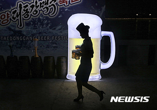 A waitress is silhouetted against an advertisement board as she carries jugs of beer during Taedonggang Beer Festival in Pyongyang, North Korea, Sunday, Aug. 21, 2016. The festival, the first of its kind in the country, was held as a promotional event for the locally brewed beer. (AP Photo/Dita Alangkara) 