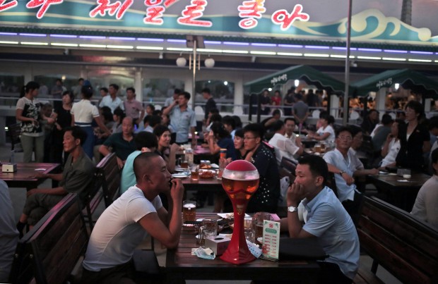 North Koreans enjoy beer and snacks during Taedonggang Beer Festival in Pyongyang, North Korea, Sunday, Aug. 21, 2016. The festival, the first of its kind in the country, was held as a promotional event for the locally brewed beer. Korean signs in the background read "Our country is the best". (AP Photo/Dita Alangkara)