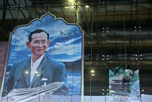 Workers move a photograph of Thai King Bhumibol Adulyadej on a window at Bangkok's International Airport Thursday, Oct. 13, 2016. Hundreds of tearful Thais were continuing to offer flowers and chant prayers on Thursday for King Bhumibol Adulyadej outside the Bangkok hospital where the world's longest-reigning monarch is being treated for multiple health problems. (AP Photo/Mark Baker)