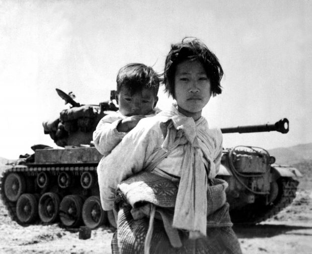 With her brother on her back a war weary Korean girl tiredly trudges by a stalled M-26 tank, at Haengju, Korea. June 9, 1951. Maj. R.V. Spencer, UAF. (Navy) NARA FILE #: 080-G-429691 WAR & CONFLICT BOOK #: 1485