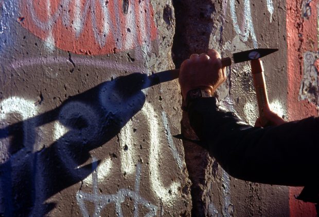 A West German man uses a hammer and chisel to chip off a piece of the Berlin Wall as a souvenir. A portion of the Wall has already been demolished at Potsdamer Platz.