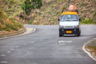 A taxi van with roof luggage speeds along a road in Bhutan