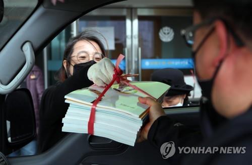 A teacher (L) of Yeongcheon Middle School in Yeongcheon, North Gyeongsang Province, hands over textbooks to a parent in a drive-thru on March 19, 2020. (Yonhap)